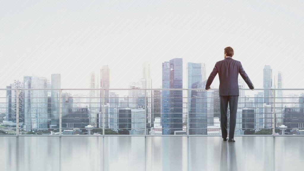 A man standing on the balcony of his apartment looking at the city.